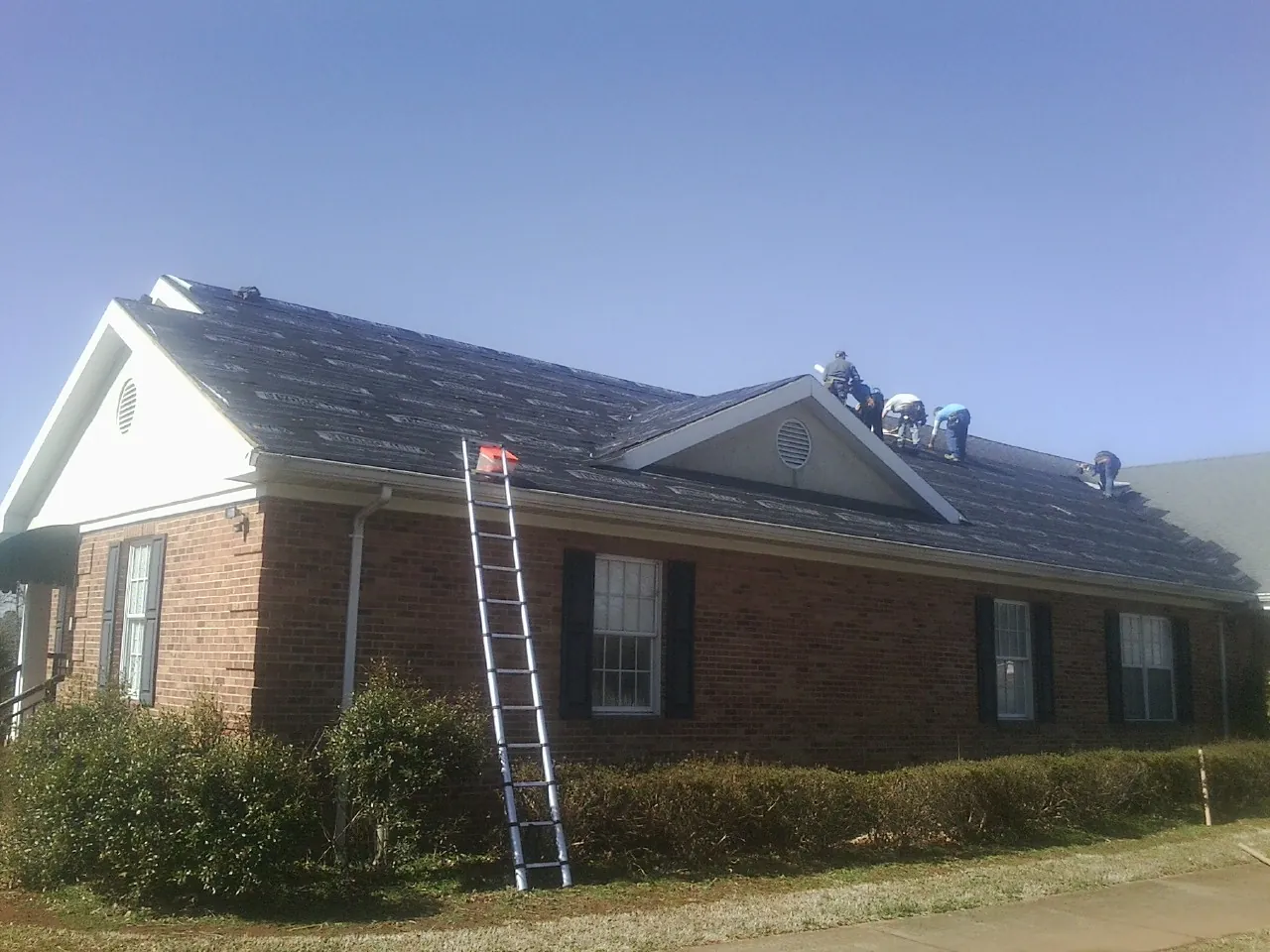 Crew tearing shingles off a brick ranch roof with a ladder set — Emergency Roof Repair work by our crew in Gamaliel