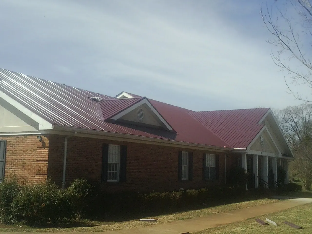 Red metal roof with gabled entries on a long brick building, from a Hail Damage Roof Repair job in Gamaliel