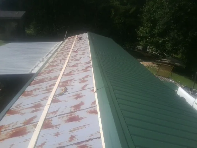Old rusted panels beside newly installed green metal roofing — Wind Damage Roof Repair by Roofing Brothers in Gamaliel