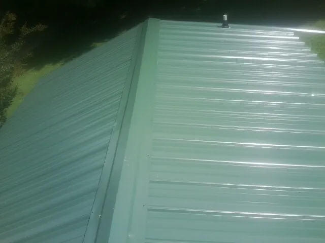 New green metal panels meeting at the ridge of a roof — Flat Roof Repair work by our crew in Gamaliel