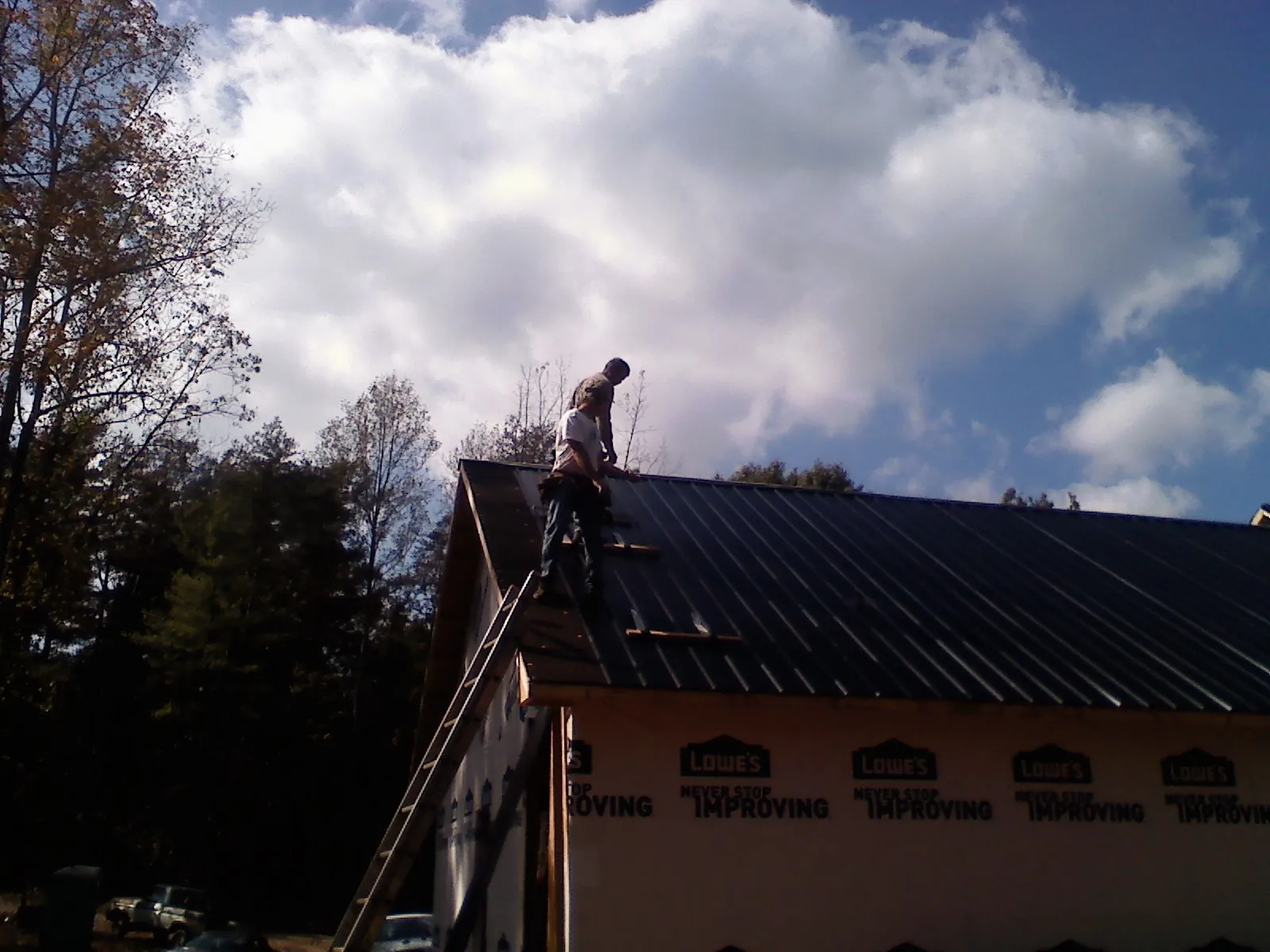 Roofer fastening dark metal panels high against a cloudy sky, from a Roof Inspection job in Gamaliel