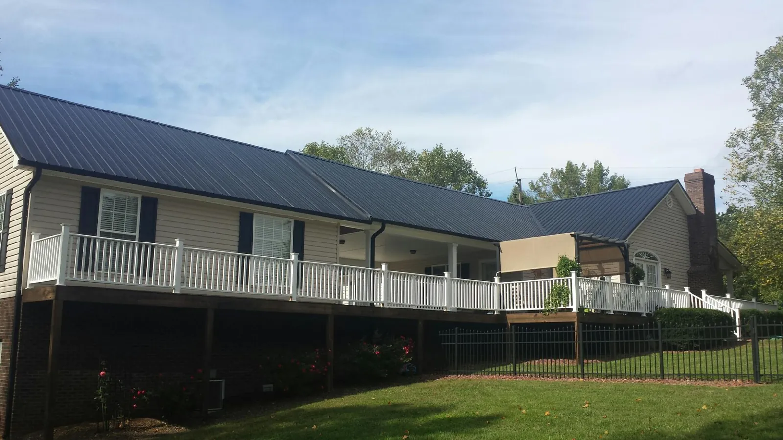 Black metal roof above a long white railed deck on a hillside home in Gamaliel