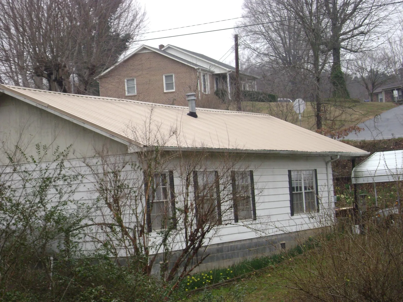 Tan metal roof on a white sided house set into a hillside — Commercial Roofing by Roofing Brothers in Gamaliel